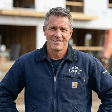 Man wearing a Summit Builders jacket in front of a construction site.