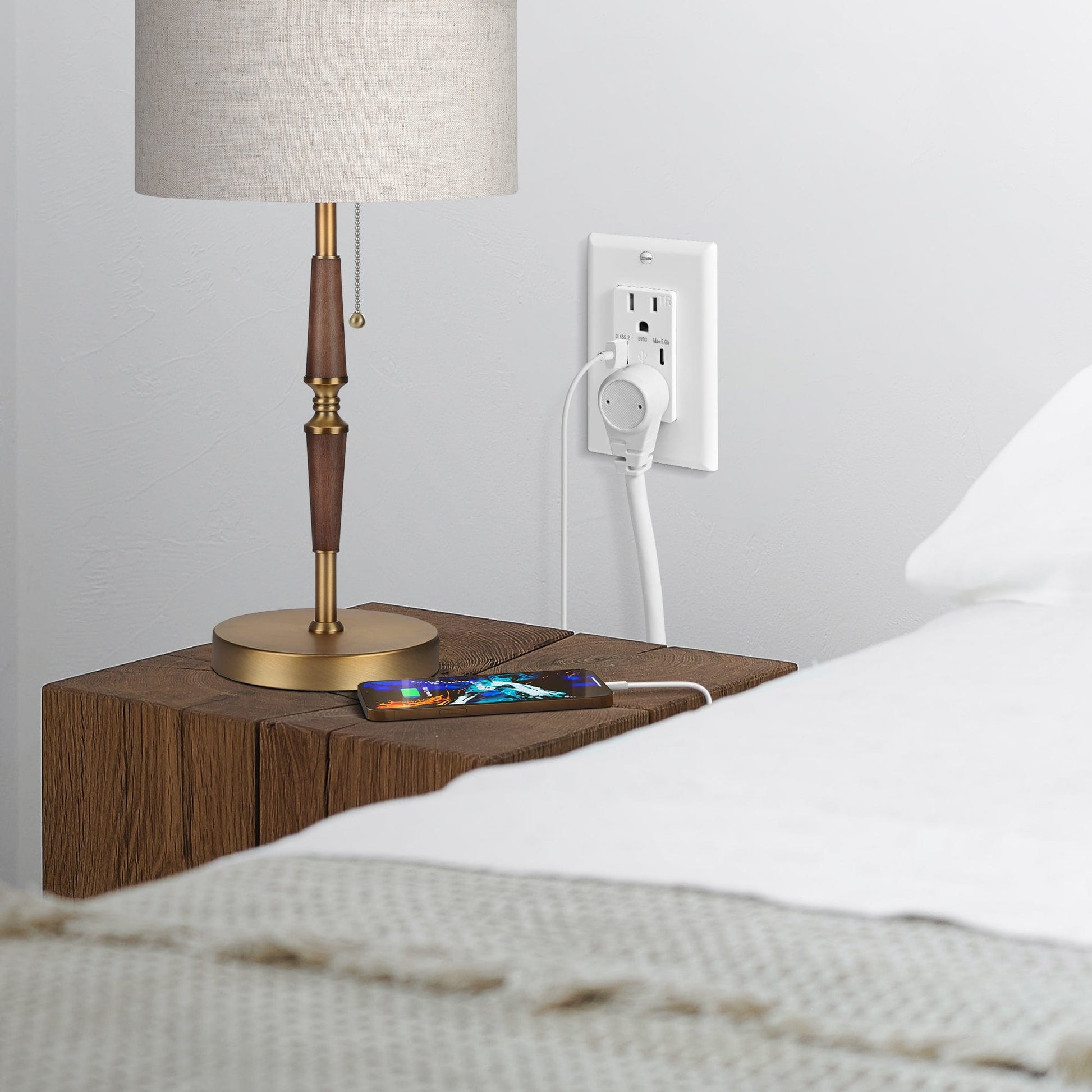 A wall outlet by the bedside powers the table lamp and mobile phone