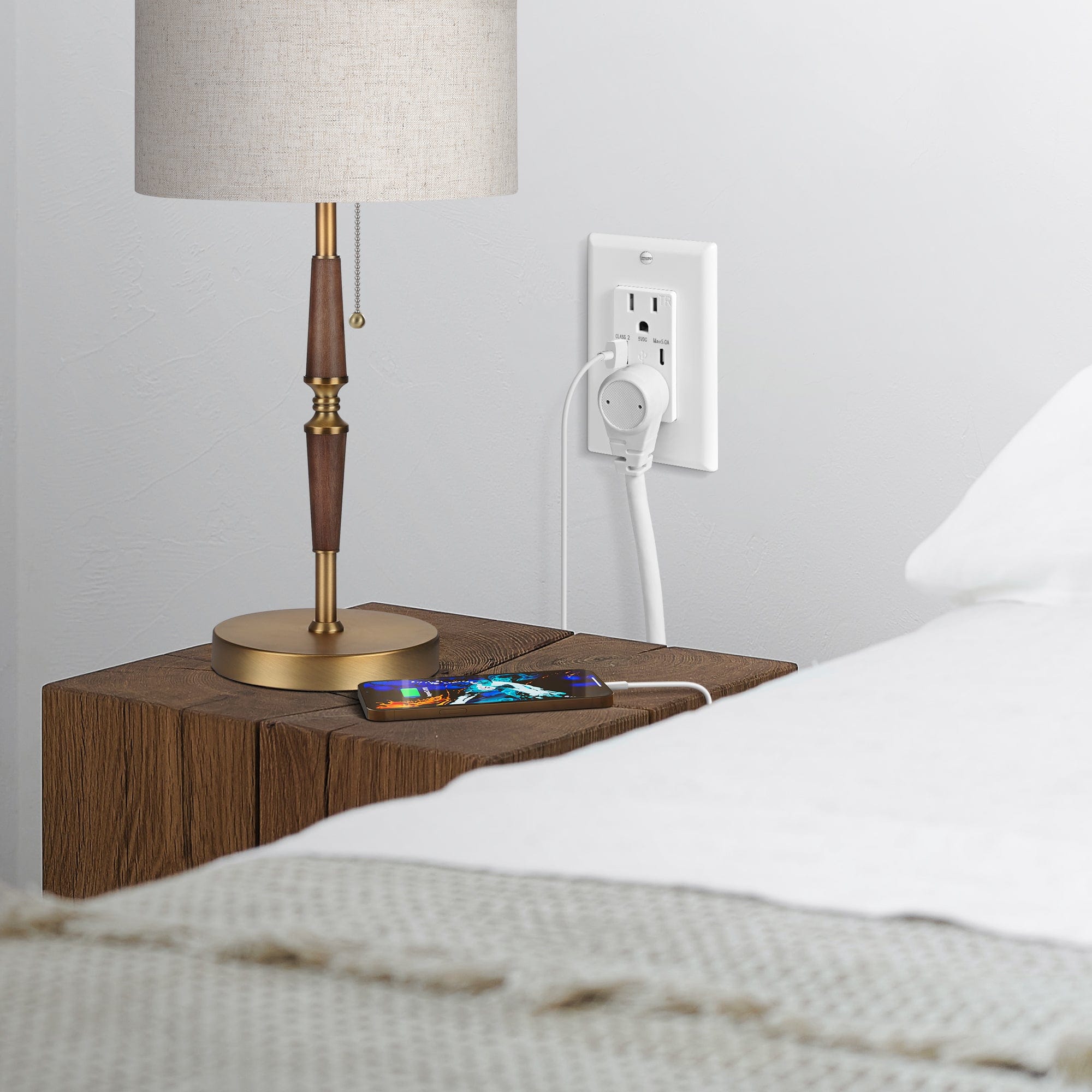 A wall outlet by the bedside powers the table lamp and mobile phone