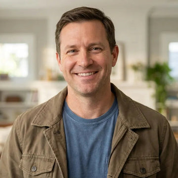 Man smiling in a home office setting with bookshelves and decor.